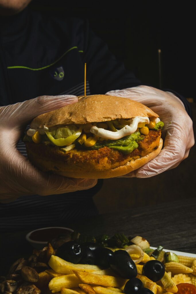 Delicious chicken burger with fries, olives, and pickles served on a table.