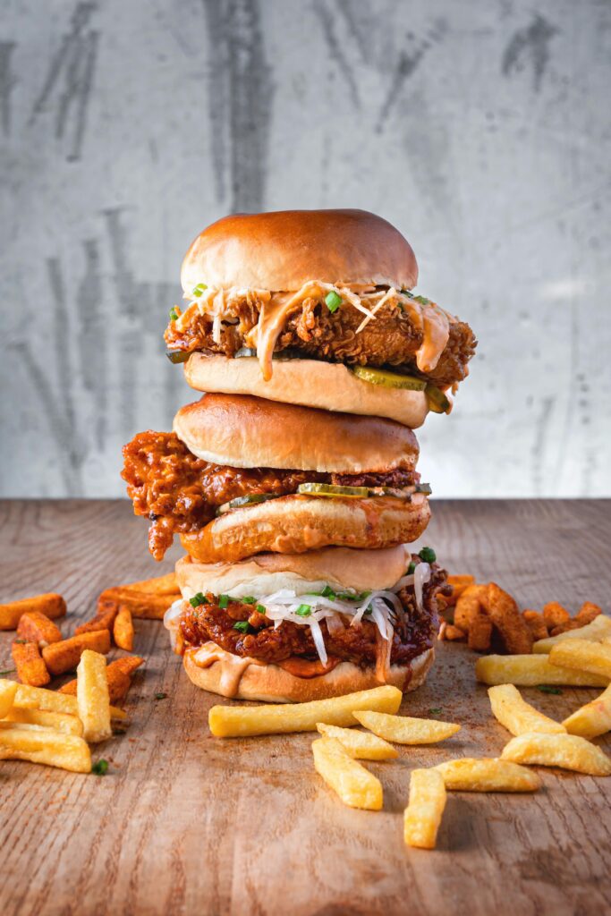 Stacked gourmet fried chicken burgers with fries on a rustic table perfect for foodie lovers.